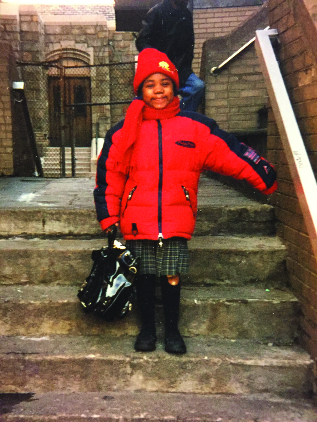 Aaliyah Hodge as a 6-year-old schoolgirl in New York. She is wearing a bright red jacket and standing on a staircase