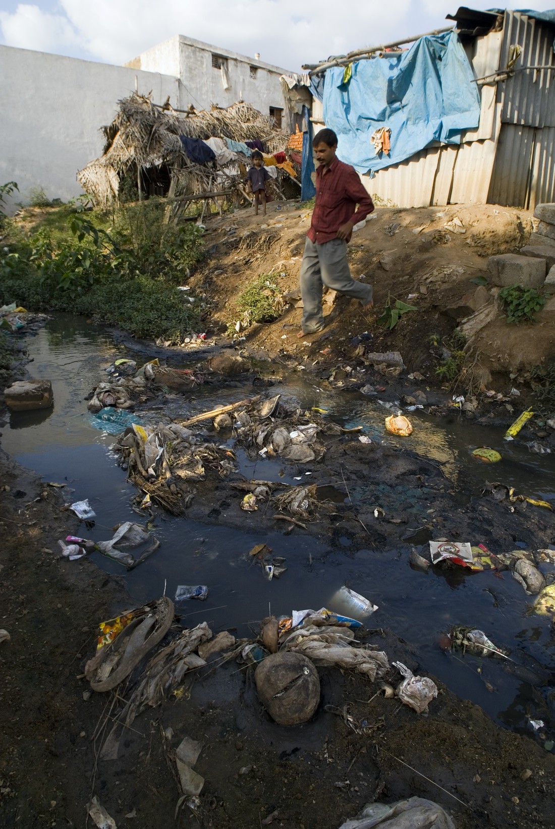 Photo of a man walking down a bank toward a stream containing garbage
