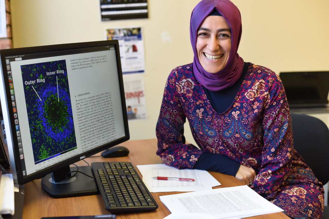 Burcin Mutlu-Pakdil, a U of M graduate student and UMD teaching assistant, next to a computer screen showing an image of the galaxy she discovered.