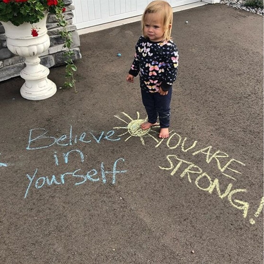 Little girl standing by chalk words Believe in yourself and You are strong!